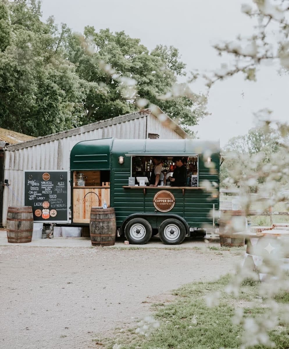 The Copper Box Events horsebox bar with chalkboard menu and barrels at a rustic outdoor event